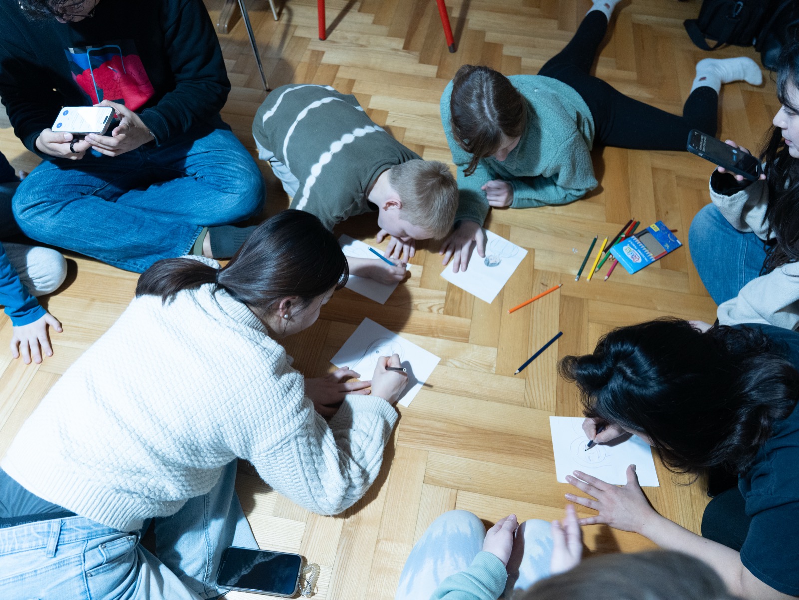 DTS students sitting together on the floor during an outreach activity, drawing and writing