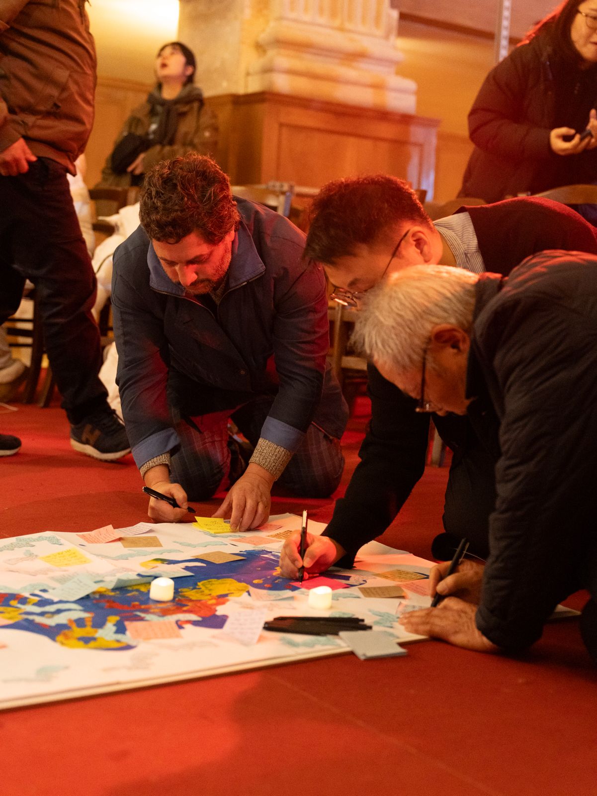 People kneeling and writing prayers on a large painted canvas on the floor of a church during intercession
