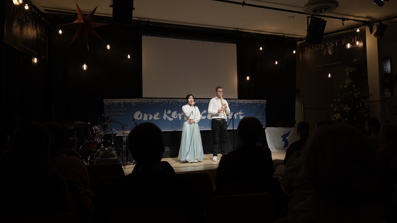 Korean and Western performers on stage at a One Korea Concert, audience silhouettes in warm light